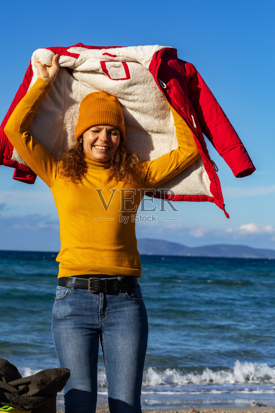 快乐的年轻女性在阳光明媚的日子里脱下外套，背景是海洋和天空。照片摄影图片