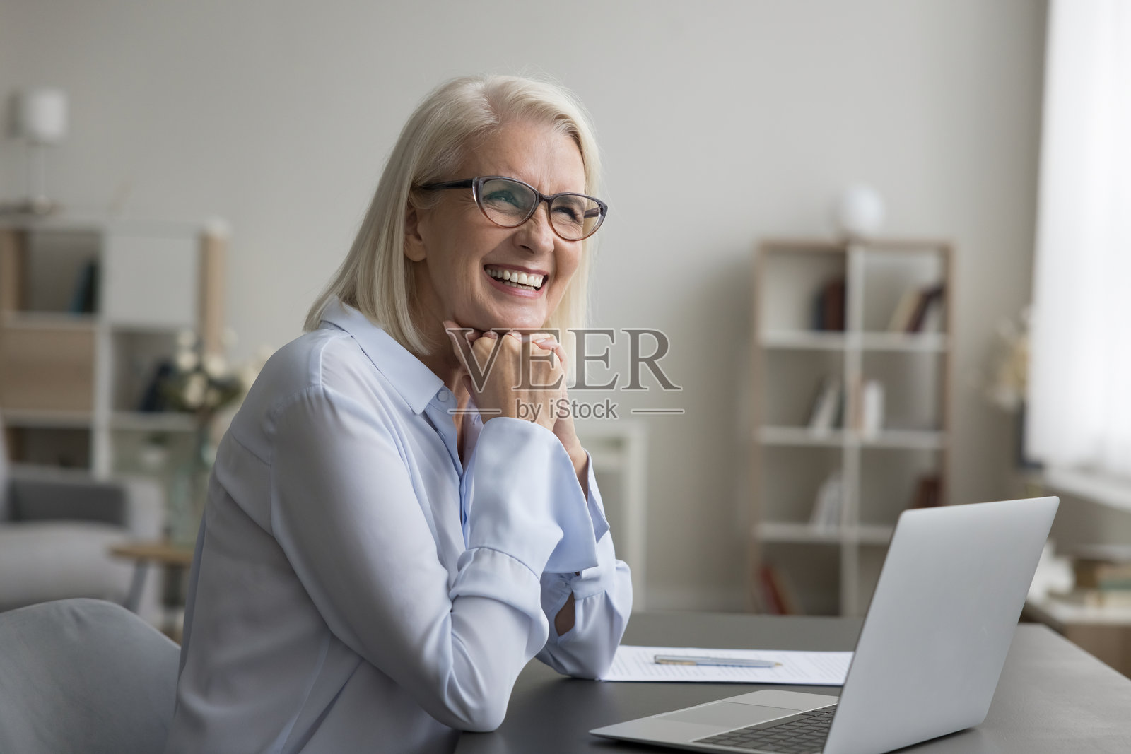 快乐成功的年长女商人在办公室的桌子前坐着照片摄影图片