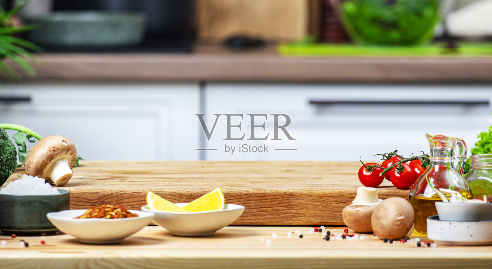 健康的素食饮食、烹饪、食品博客横幅背景。空的橡木砧板上放着蘑菇、西红柿、蔬菜和香料，背景是温馨的厨房，配有厨房用具和器皿。照片摄影图片