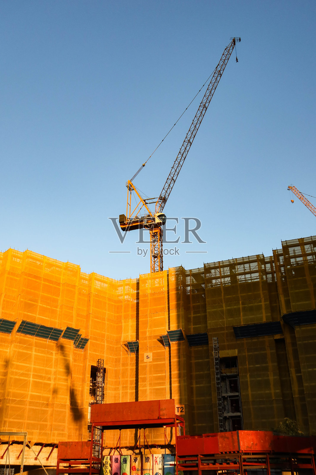 傍晚时分，蓝天映衬下，正在建设中的住宅楼群特写，塔吊和黄色安全网清晰可见。照片摄影图片