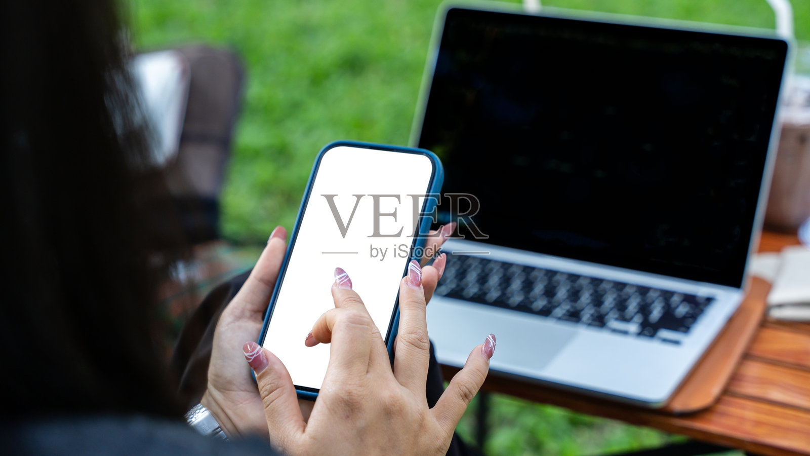 阳光明媚的日子里，女性手部特写，正在公园里使用手机和笔记本电脑。照片摄影图片