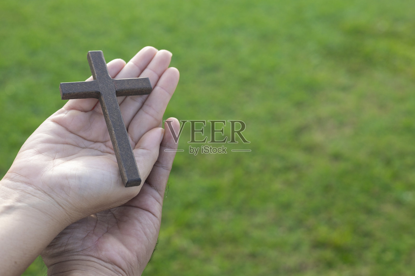 一对手握着木制十字架，祈祷信仰，奉献，基督教，希望与和平，神圣的十字架，绿色草地，灵性，宁静，自然的重生与和谐。耶稣受难日复活节。照片摄影图片