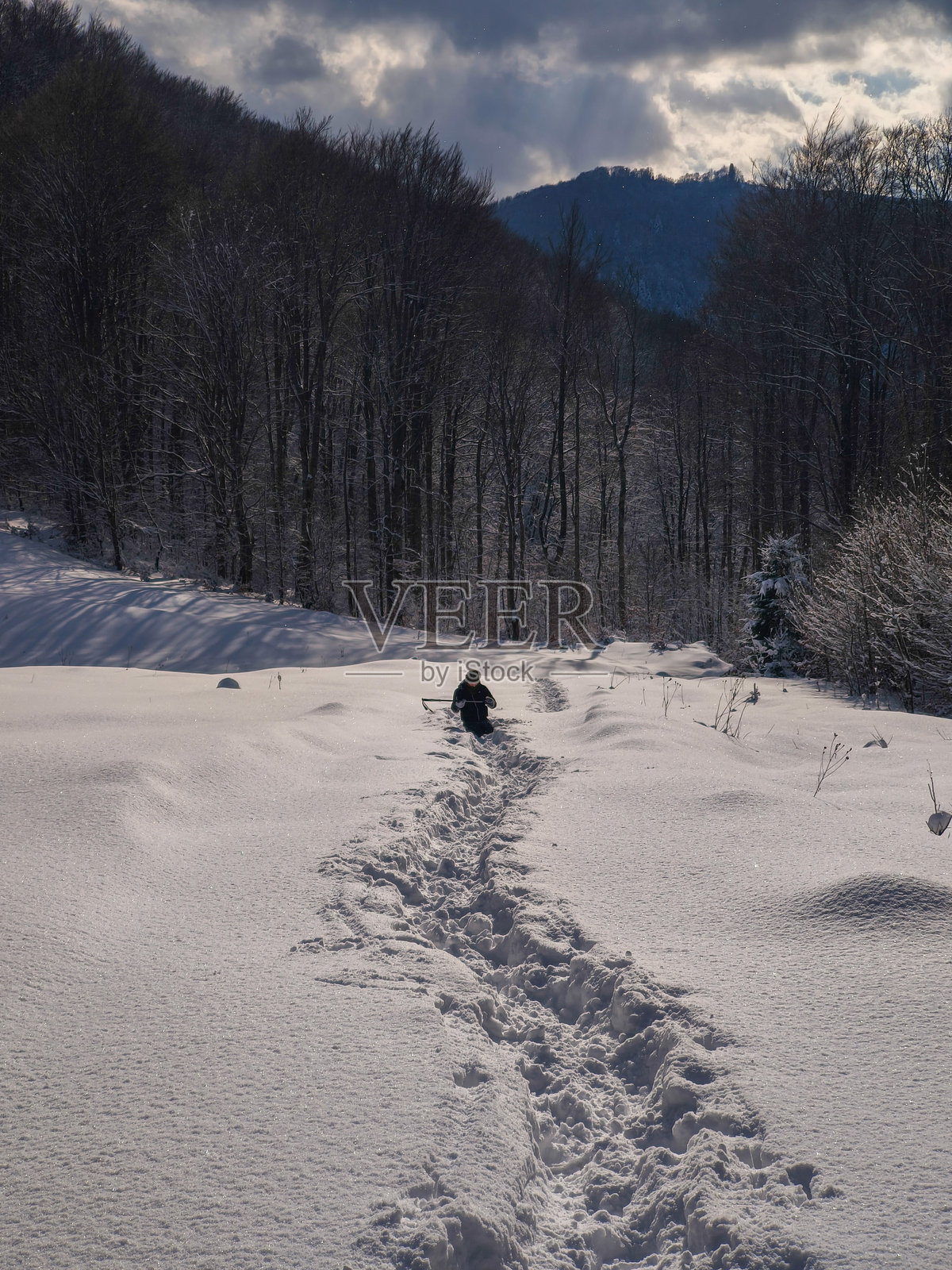 一个男人在深雪中行走，踩出一条小路。照片摄影图片