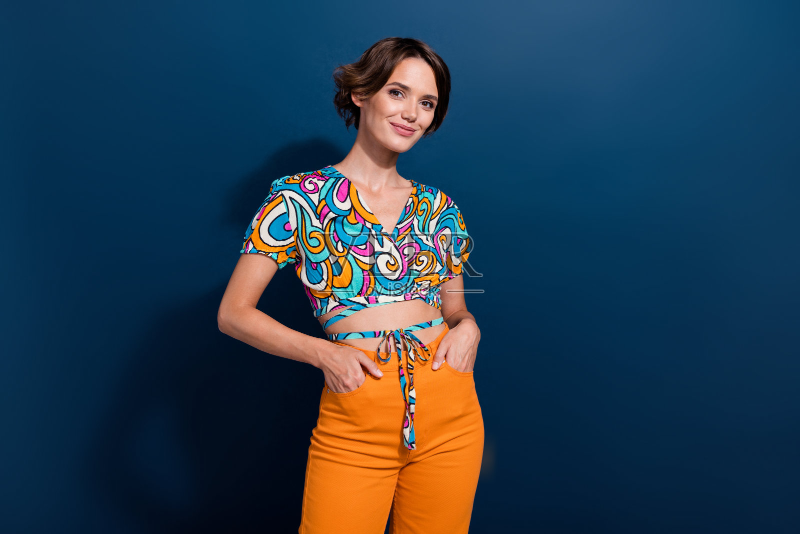 年轻漂亮的女士将手放在口袋里，摆姿势为《时尚》杂志拍照，身穿复古夏季服装，背景为蓝色。照片摄影图片