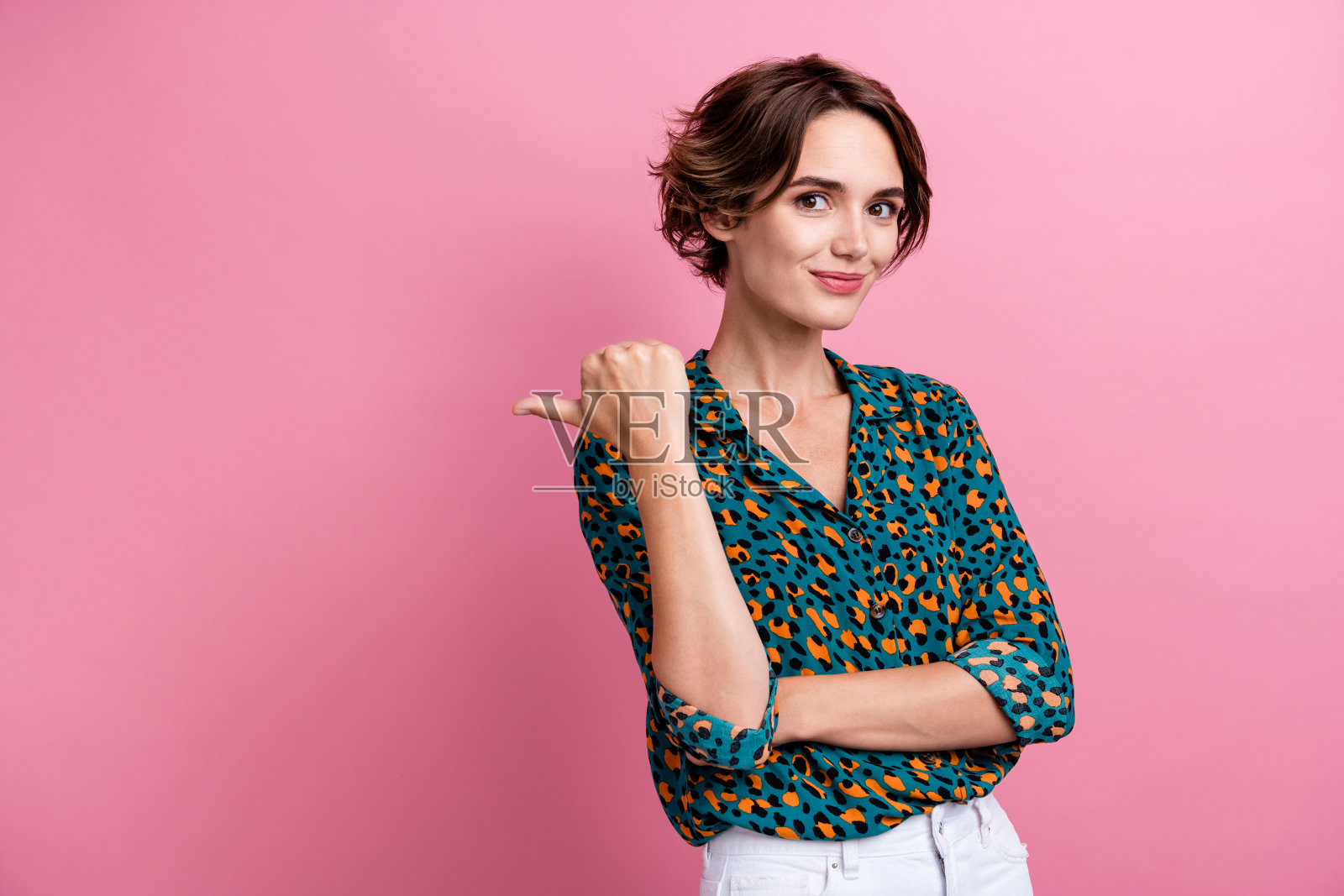 可爱的积极女孩，留着波波头，穿着时尚衬衫，指向粉色背景上空的优惠空位。照片摄影图片