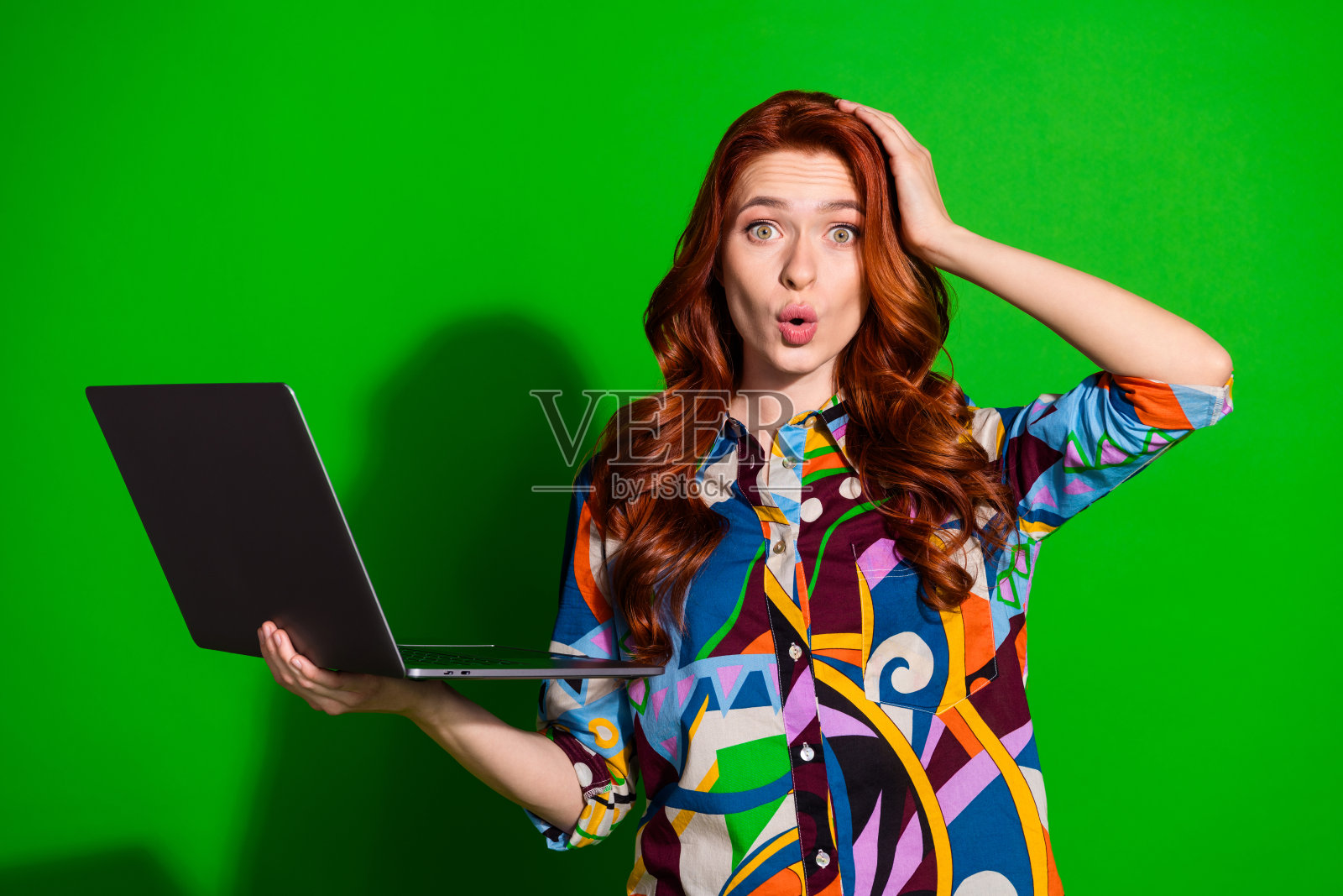 年轻女子手持笔记本电脑，背景为鲜艳的绿色照片摄影图片