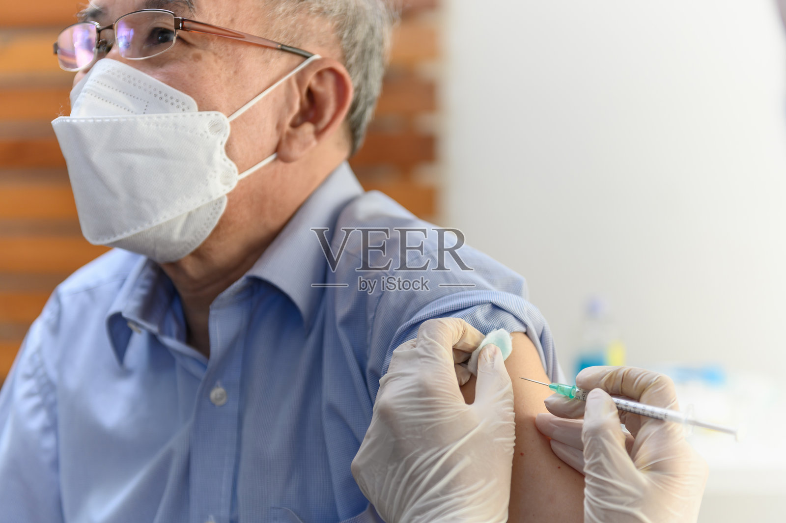 亚洲女性护士在诊所或医疗中心为戴口罩的泰国老年男性患者注射新冠疫苗的特写镜头。新冠病毒疫情防护或医疗健康概念。照片摄影图片