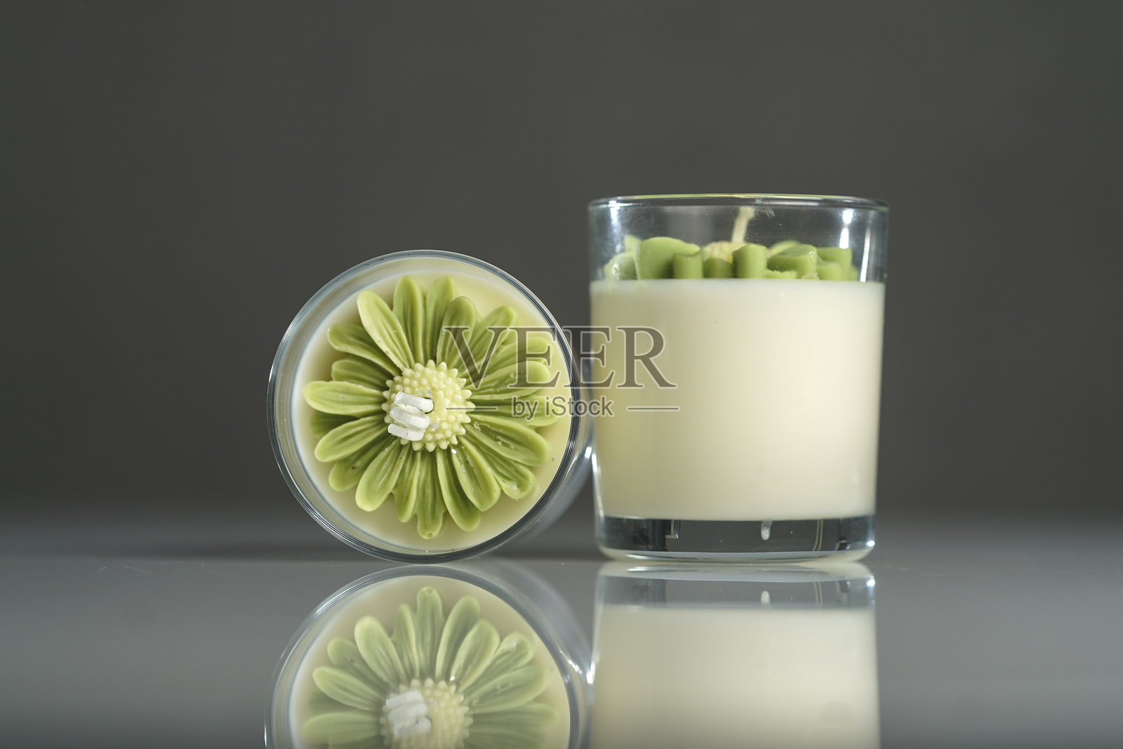 透明玻璃罐中装有绿色花朵的手工蜡烛，背景为灰色照片摄影图片