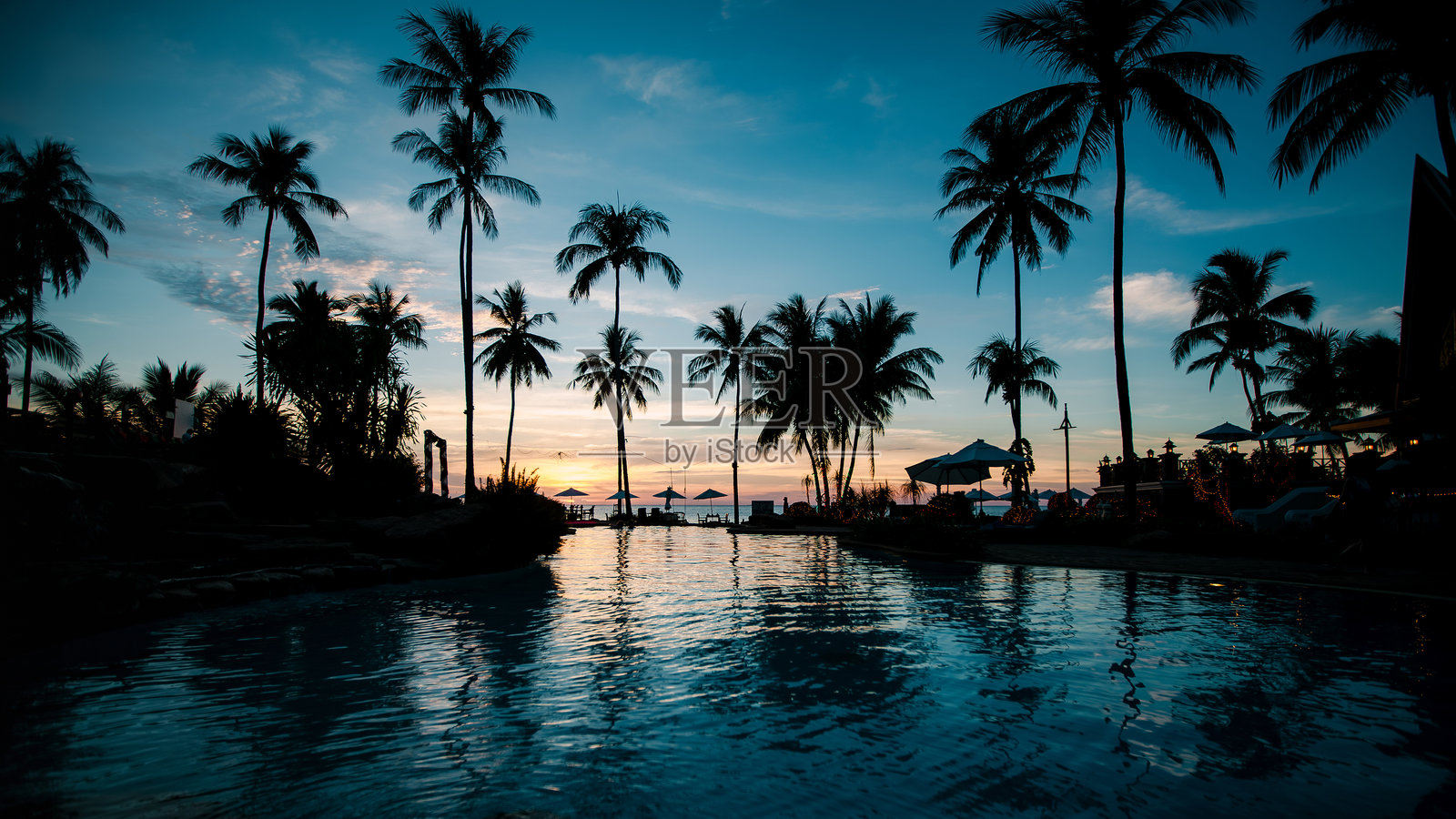 热带海滩上棕榈树的剪影映照在水面上，沐浴在令人惊叹的日落光辉中。照片摄影图片