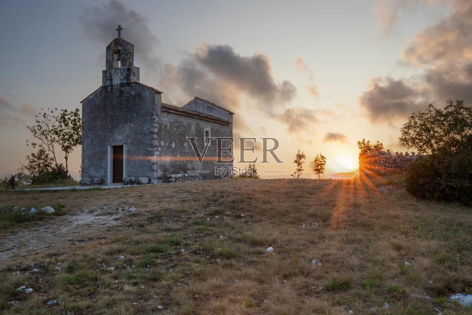 美丽的小教堂坐落在海边，日出时分的风景。逆光拍摄，能看到太阳，克罗地亚布雷斯克。照片摄影图片