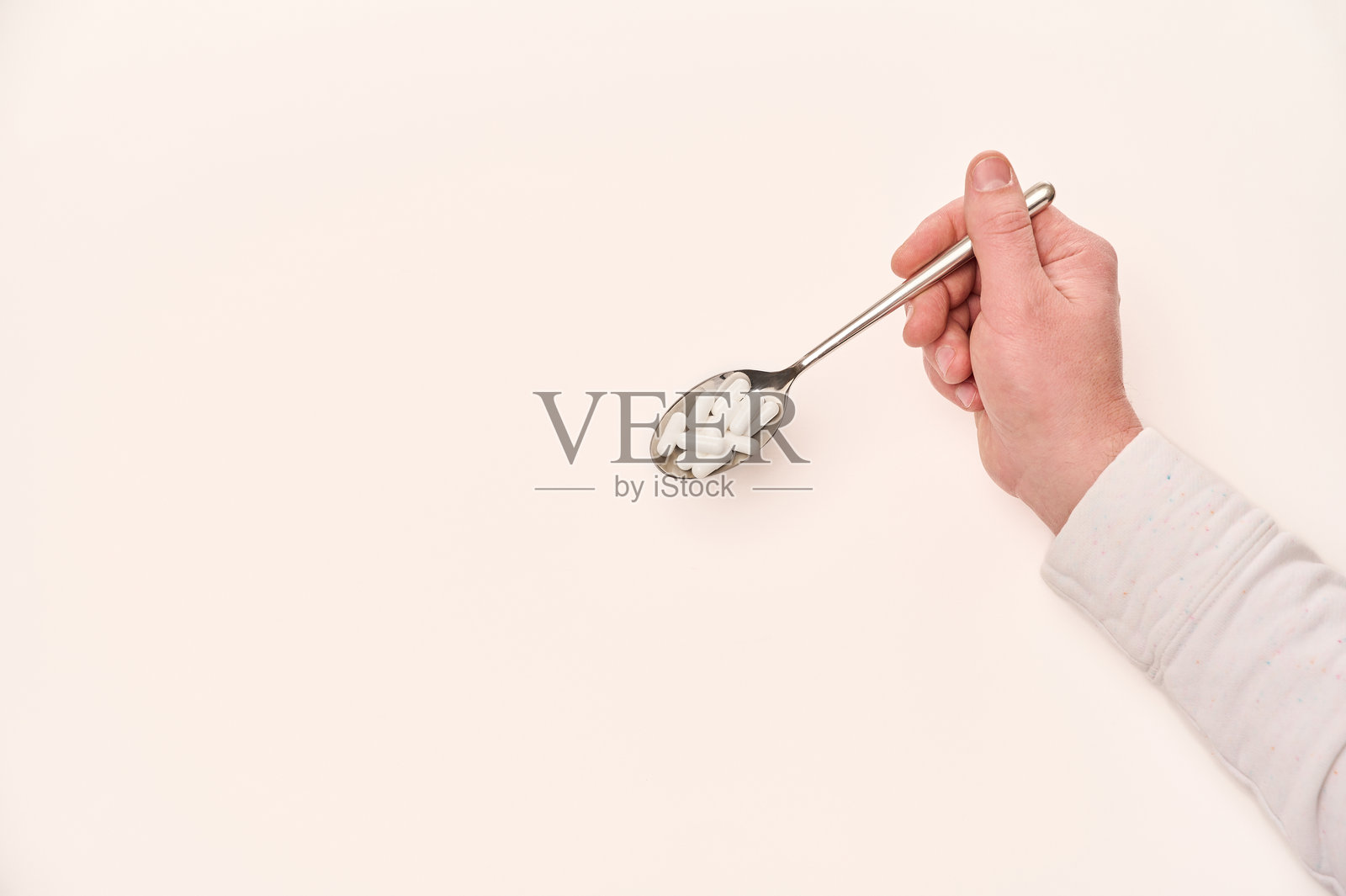 手握银色勺子，勺上放着糖块，背景为明亮的厨房环境。照片摄影图片