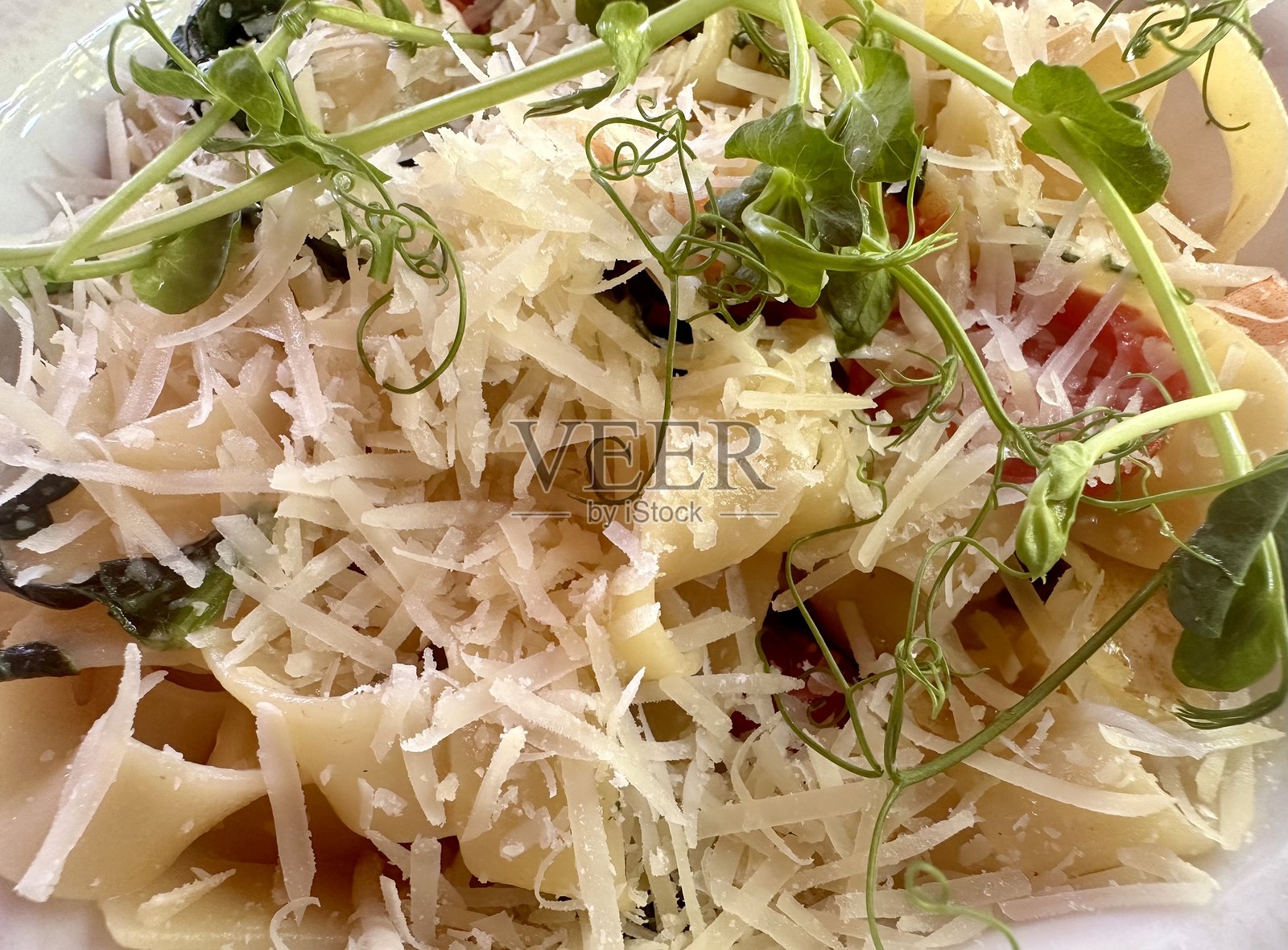 优雅的意大利面菜肴，采用新鲜的宽面条、磨碎的帕尔马干酪、生机勃勃的绿叶蔬菜和多汁的樱桃番茄，精美摆盘，呈现完美的美食风格。照片摄影图片