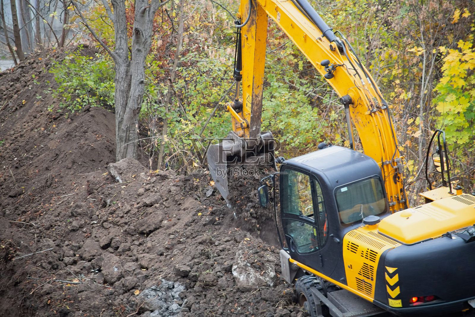 挖掘机在树木环绕的建筑工地上填土。照片摄影图片