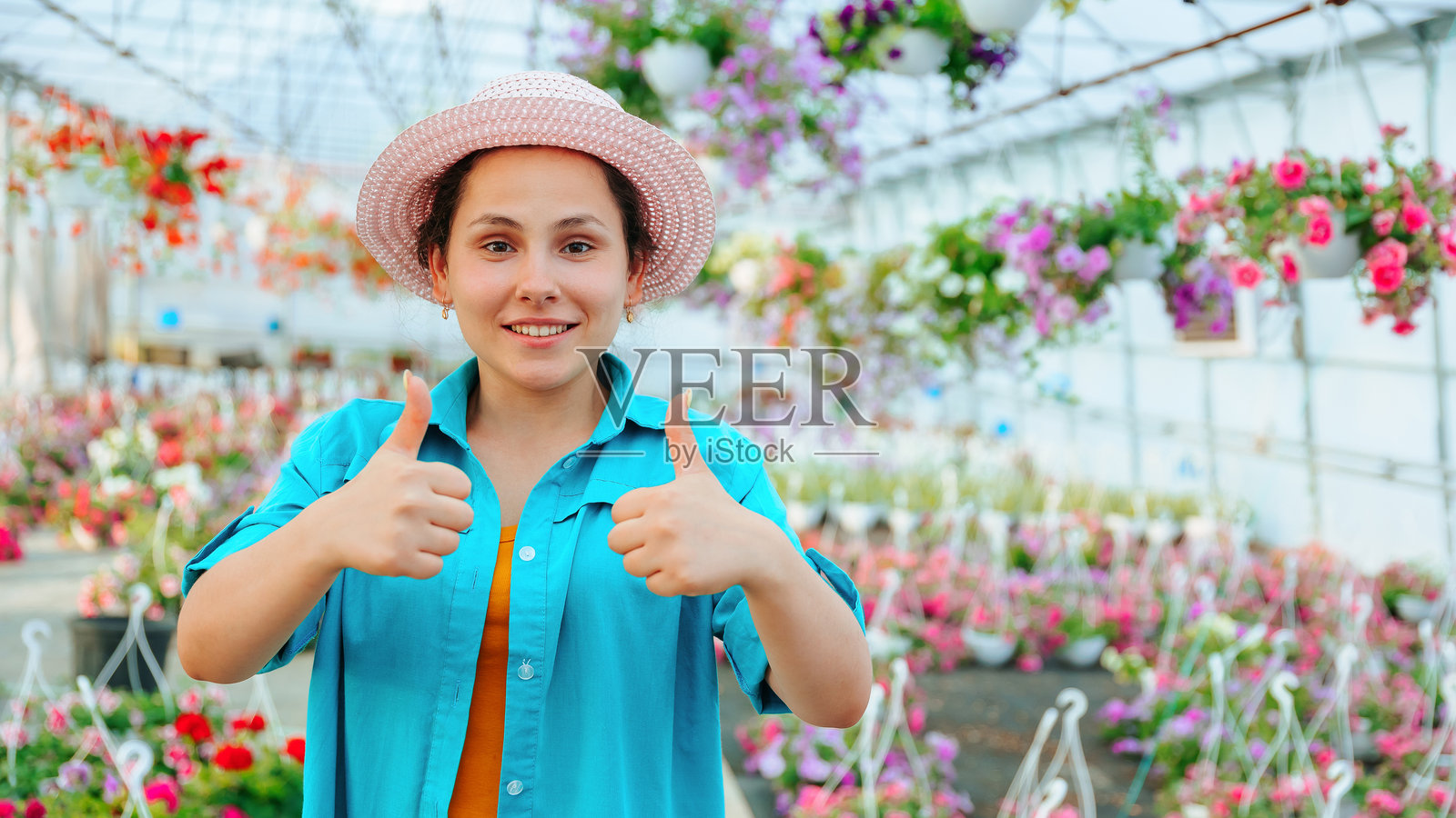 美丽的女人站在温室里，面带微笑，朝着镜头看。照片摄影图片