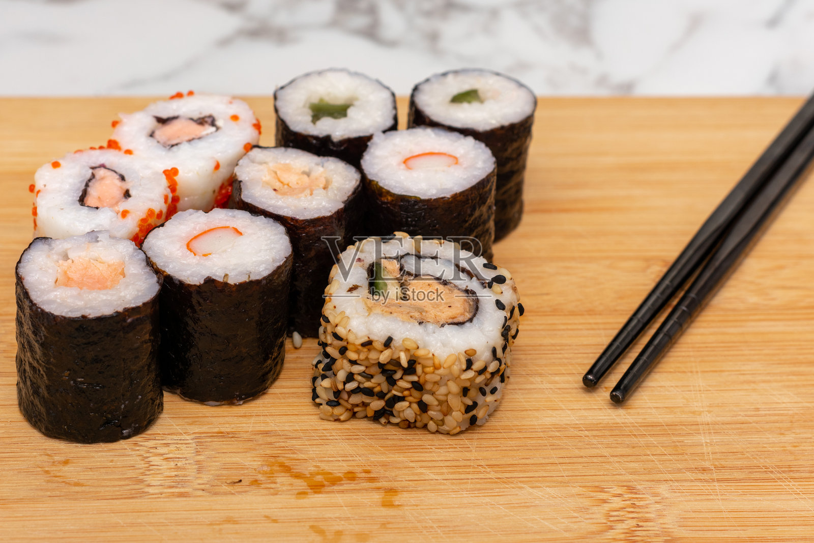 木板上摆放着各种寿司卷。这些寿司卷颜色和大小各异，旁边有一双筷子。多样性和丰盛的概念。照片摄影图片