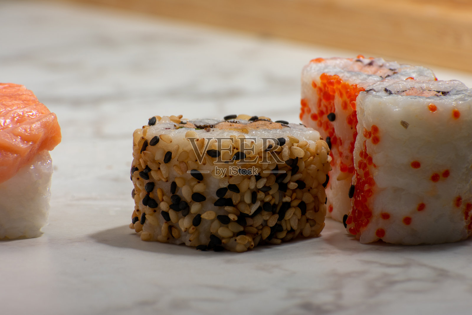 寿司卷静置在白色表面上，配有多种配料，包括三文鱼、芝麻和鲜艳的橙色鱼子，形成了一个色彩丰富且诱人的展示。照片摄影图片