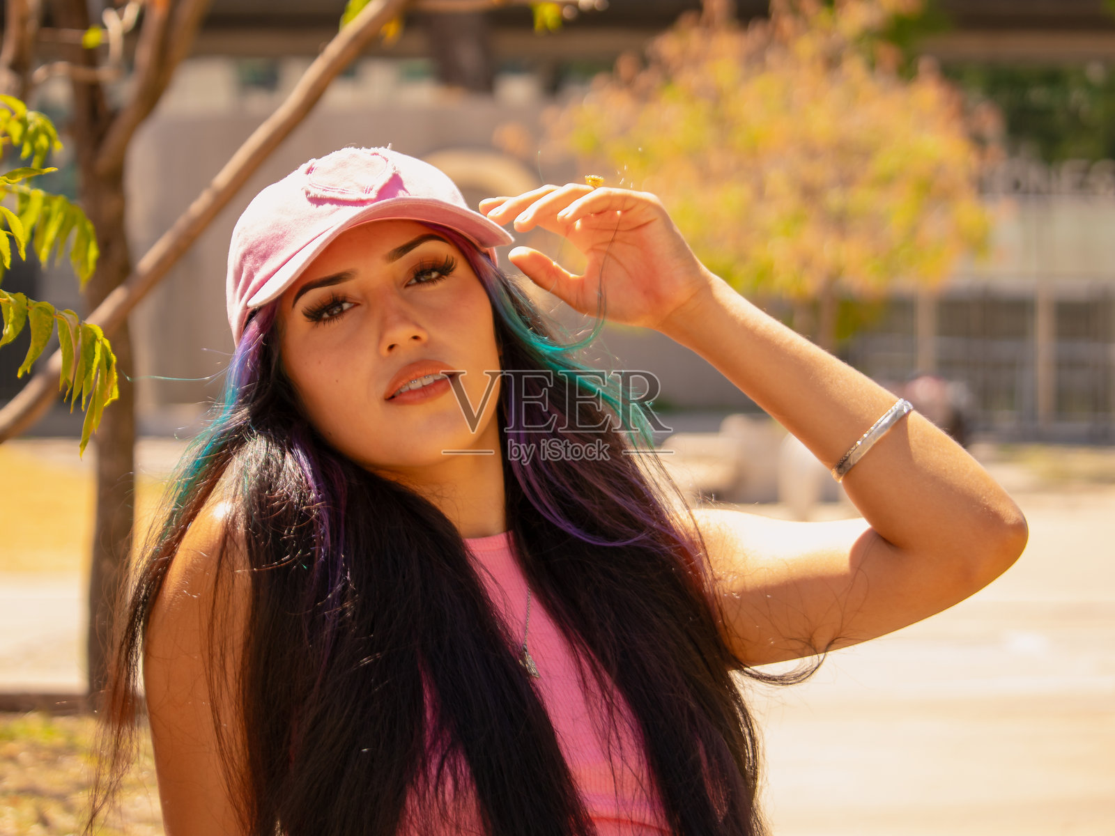 年轻的拉丁裔女性，戴着粉色帽子，长发披肩，在阳光明媚的日子里显得很严肃。照片摄影图片