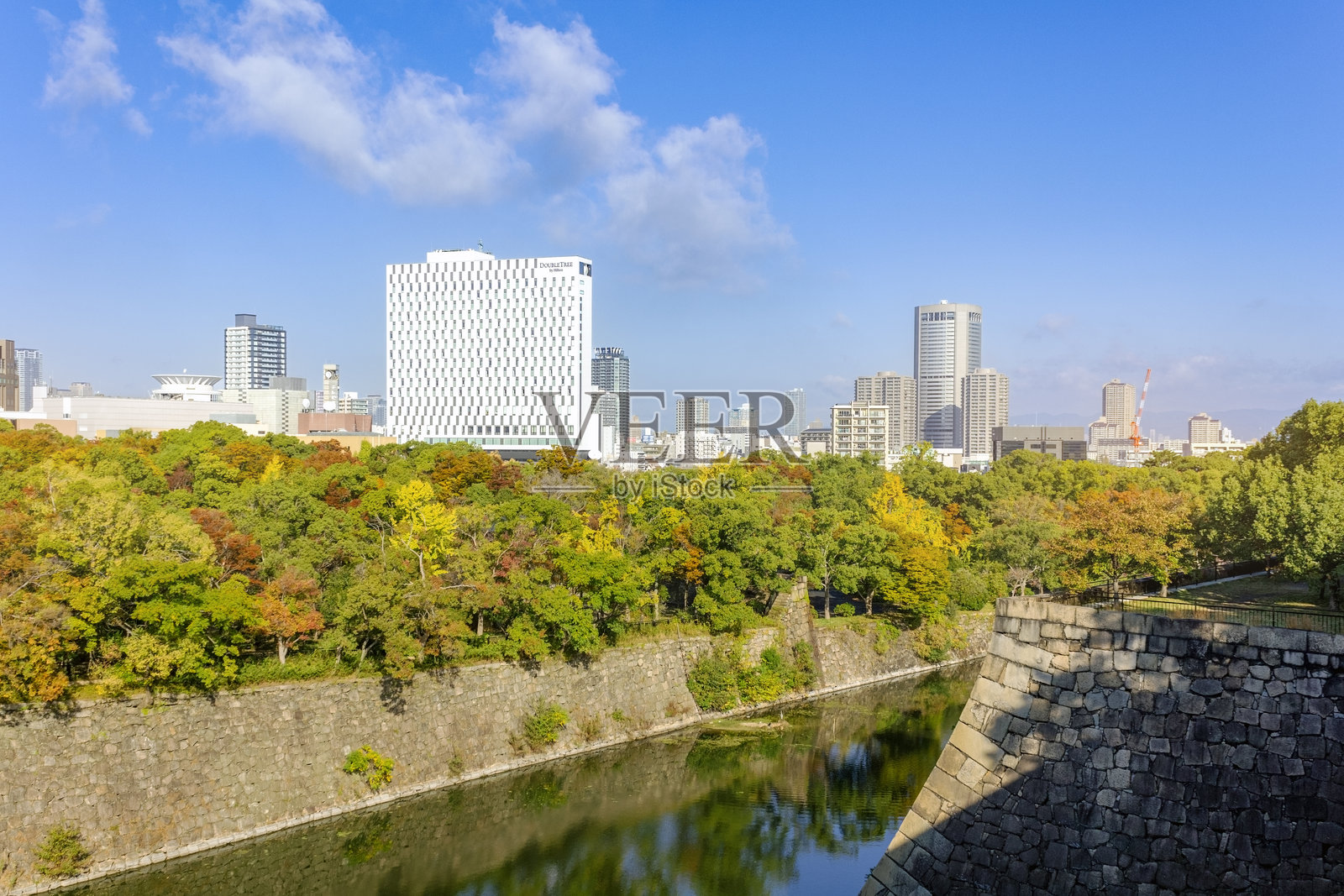 日本大阪的风景,展示了郁郁葱葱的绿意、古老的大阪城石墙和现代城市天际线的结合。照片摄影图片