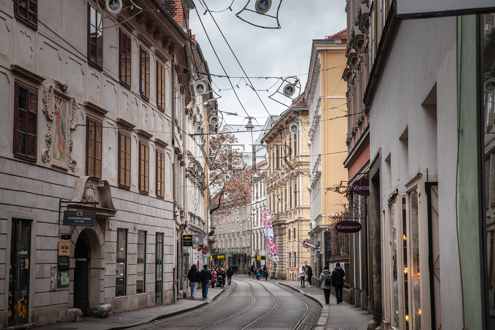 格拉茨的纽托尔街展现了历史悠久的建筑立面、节日的悬挂灯饰和宁静的电车路线。路过的行人探索着这个城市走廊中的商店和咖啡馆。照片摄影图片
