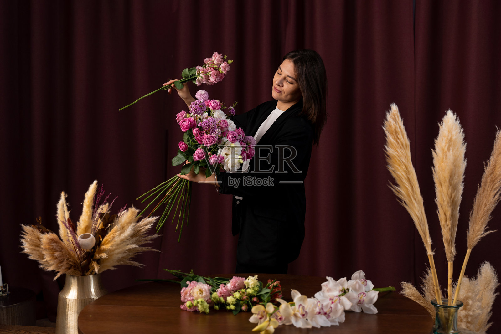 女花店老板正在为客户制作花卉装饰，组装花束。女性花艺师在深色背景下组装花束。照片摄影图片