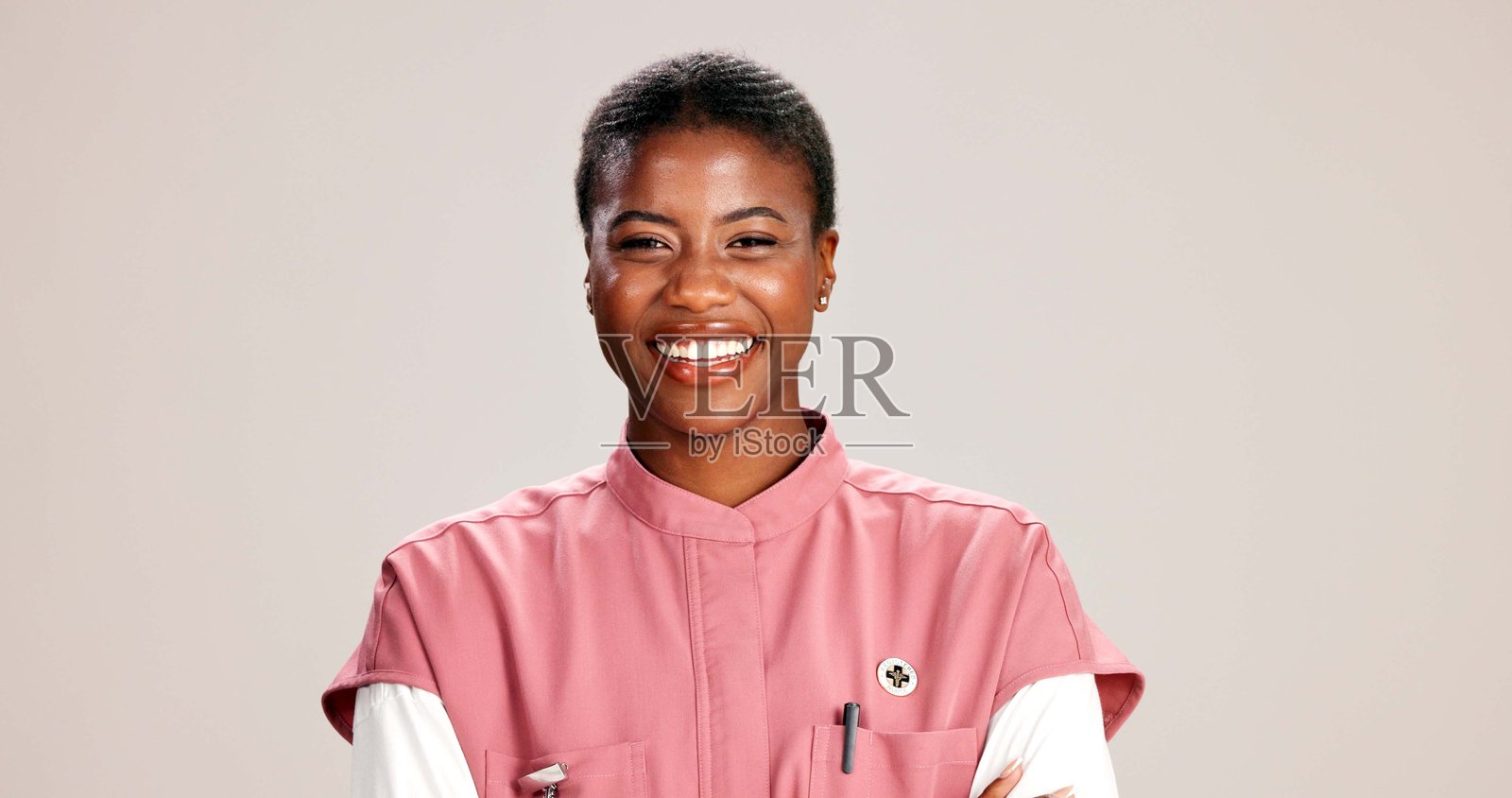 微笑的黑人女性医生在工作室的肖像，展现职业自豪感或自信，背景为白色，双臂交叉，代表医疗服务，心脏病专家或快乐的形象。照片摄影图片