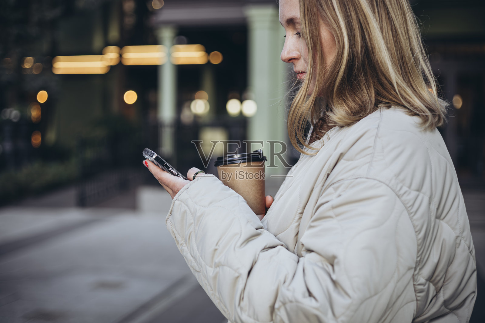 一位年轻女性在上班路上使用智能手机并喝咖啡。照片摄影图片