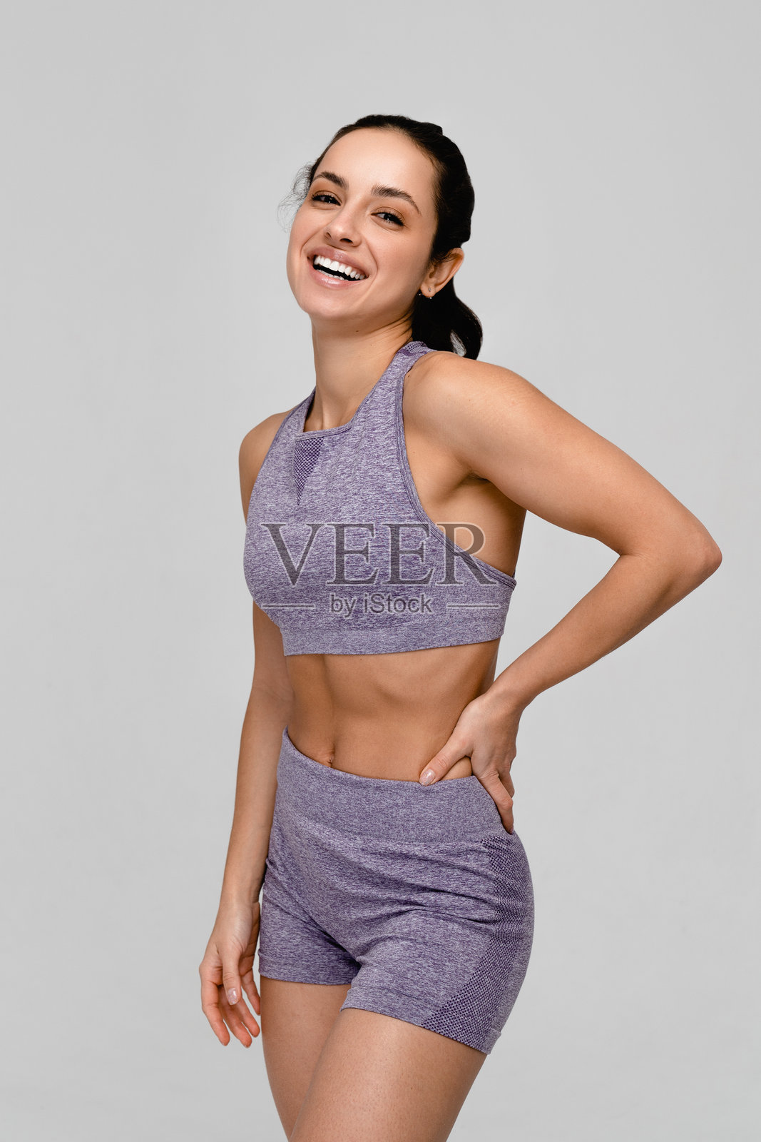 垂直拍摄的运动健身女性穿着运动服在白色背景的工作室中进行运动。照片摄影图片