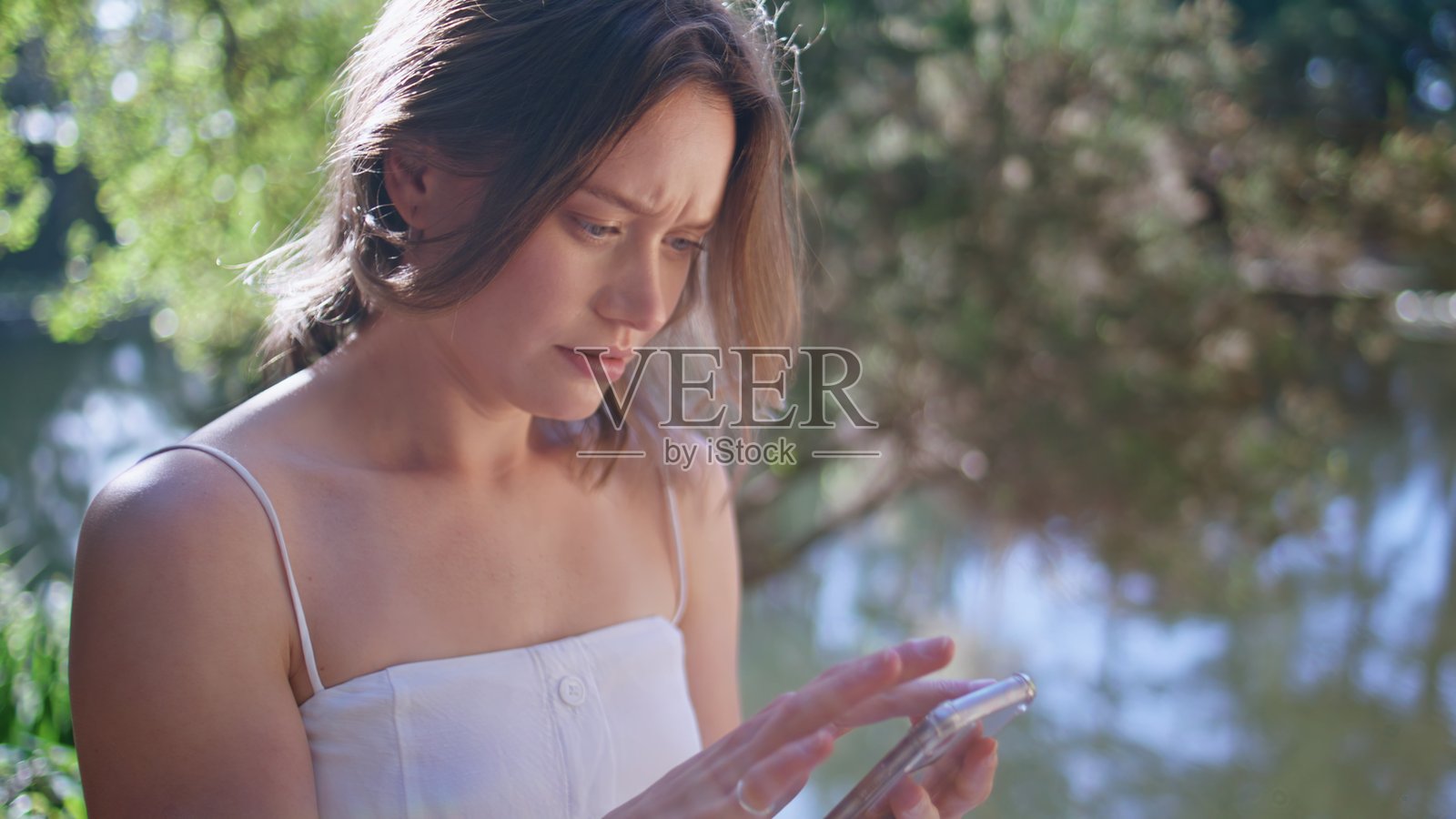 担心的女人在阳光明媚的公园里使用手机，困惑于故障的设备特写照片摄影图片