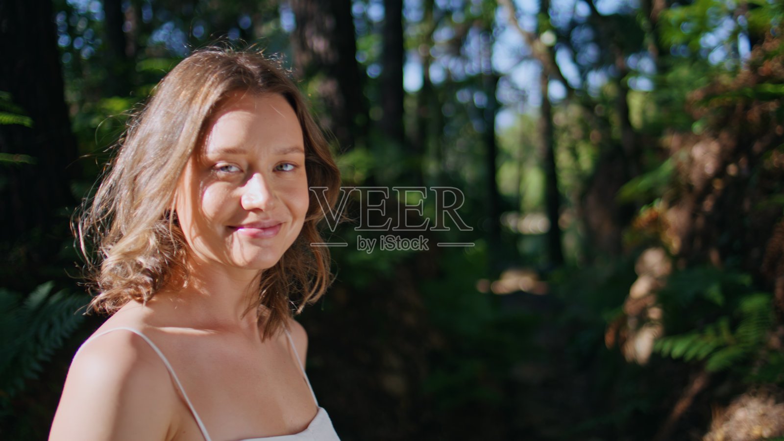 温柔的女士在阳光下沐浴，闭着眼睛，面带宁静的表情，背景是自然风光的肖像。照片摄影图片