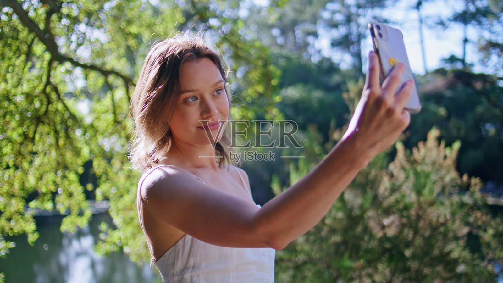 快乐的女孩在绿树环绕中摆姿势拍照。女人在自拍。照片摄影图片