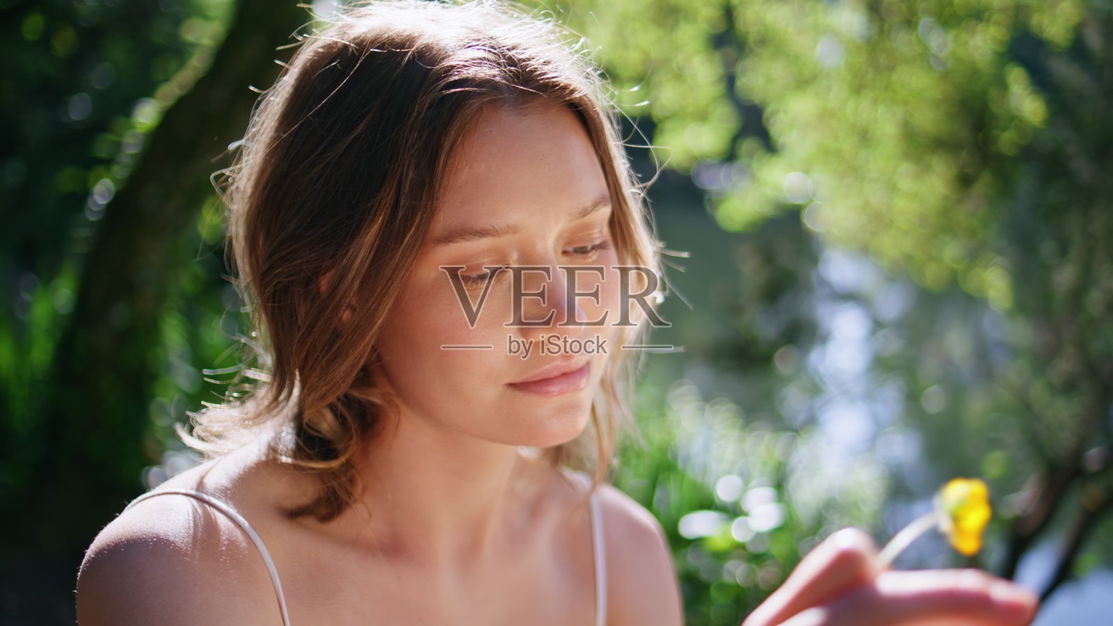 温柔的女孩在阳光明媚的夏季花园中阅读书籍特写。女人手中拿着花。照片摄影图片