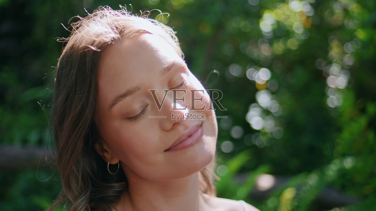 年轻女性在阳光下沐浴，闭着眼睛，面带宁静的表情，特写镜头。照片摄影图片