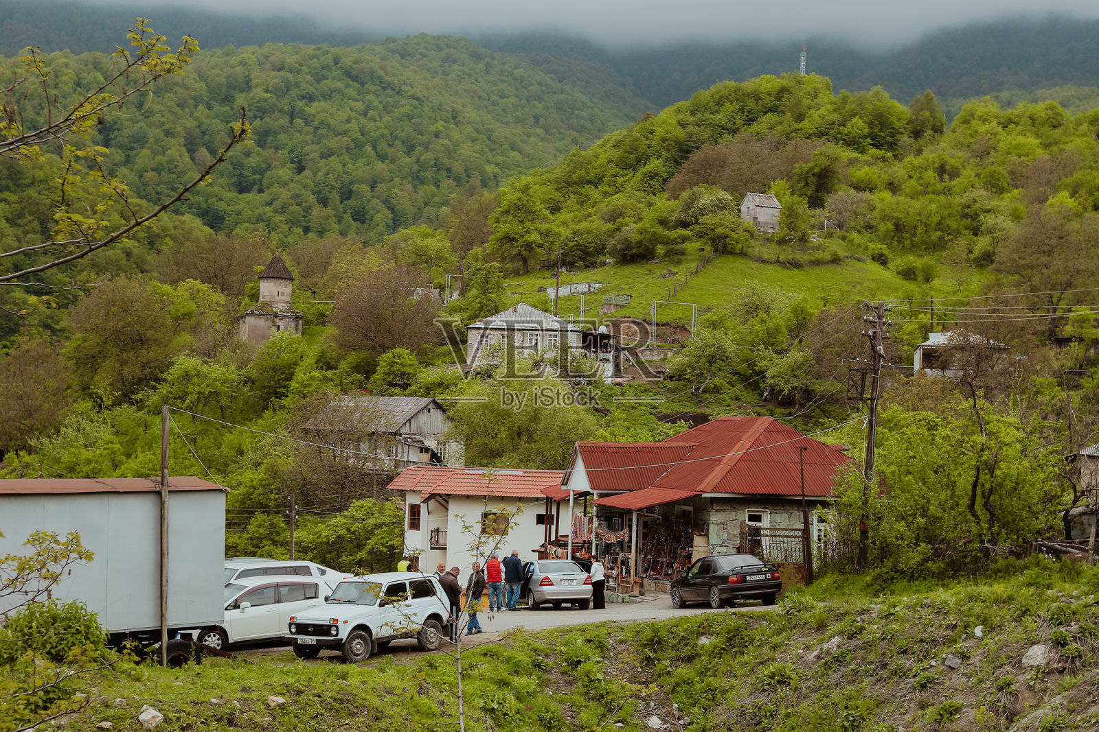 游客们在一个被郁郁葱葱的山丘环绕的小亚美尼亚村庄聚集,天气阴云密布。照片摄影图片
