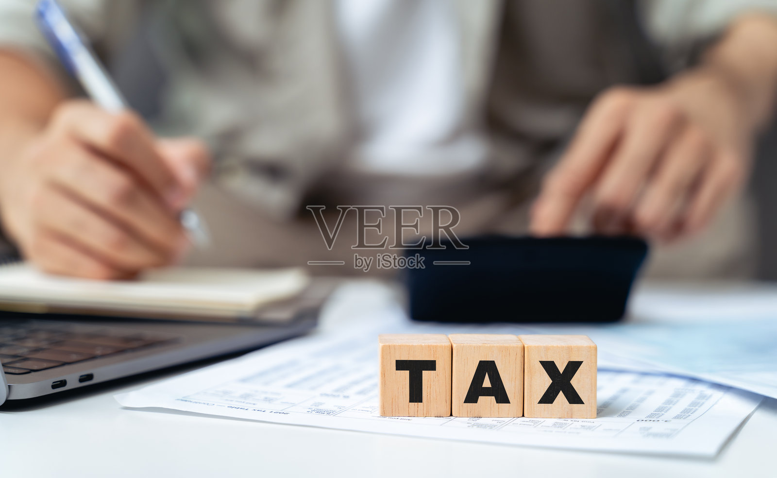 男子正在用计算器计算年度税款，木块上写着“税”字。照片摄影图片