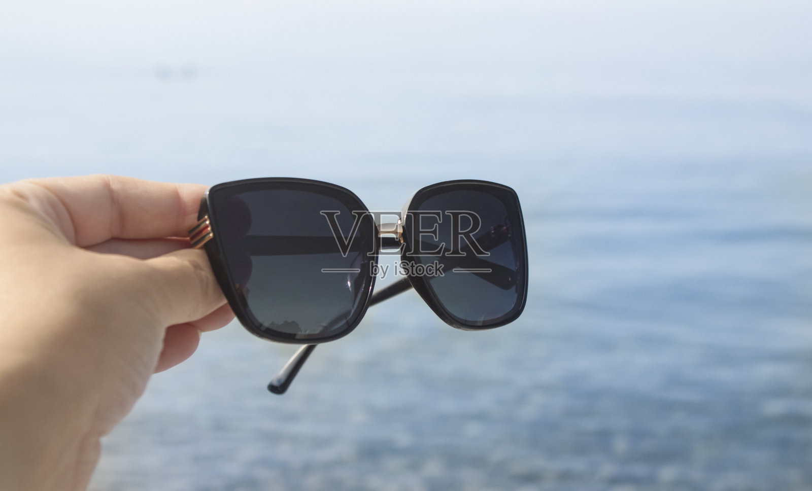 一只手在海边的夏日里拿着时尚的太阳镜。夏日氛围。照片摄影图片