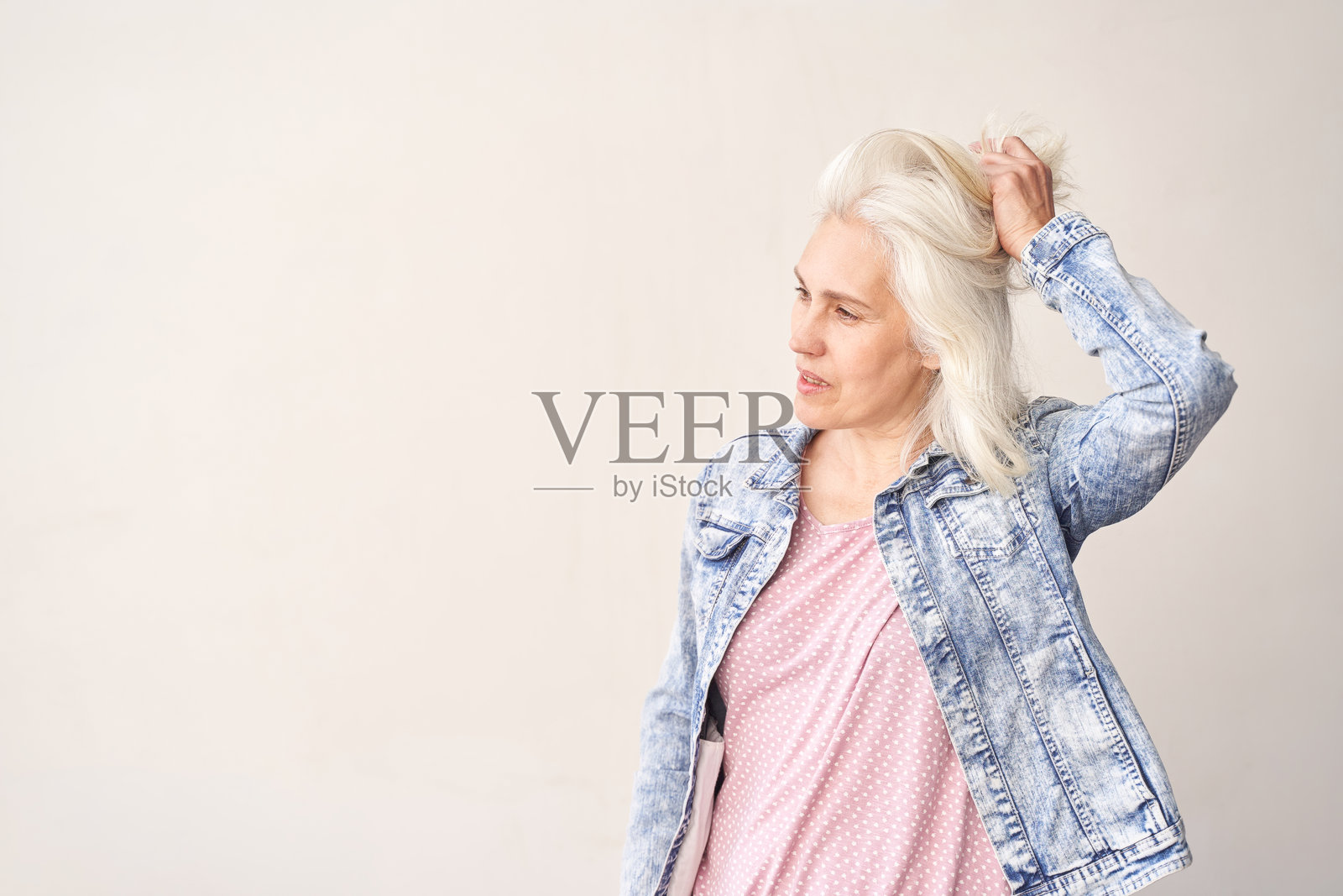 时尚的银发老年女性穿着牛仔夹克，背景为中性色调照片摄影图片