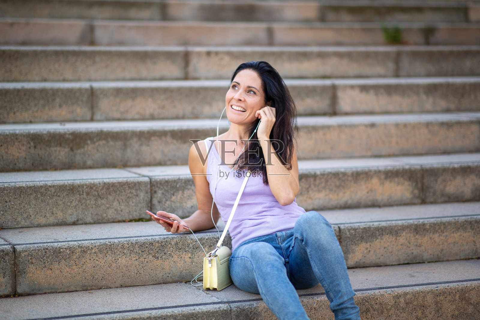 女人坐在城市的台阶上放松，使用手机和耳机听音乐照片摄影图片