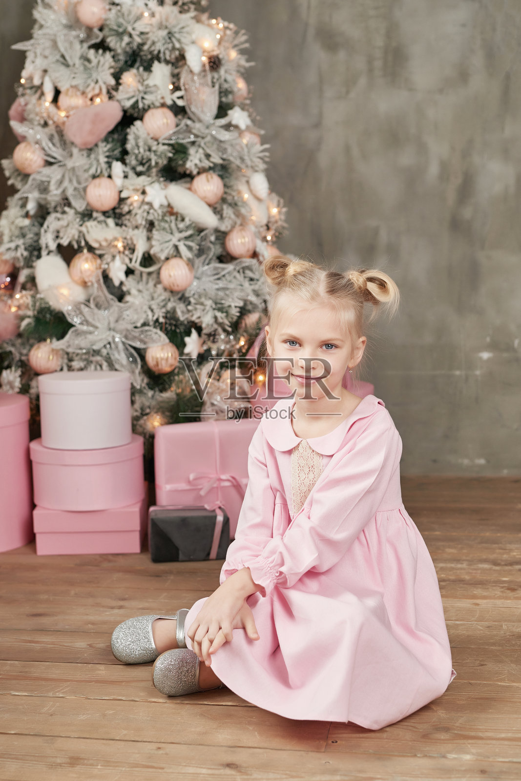 穿着粉色裙子的小女孩在圣诞树前拿着礼物。圣诞快乐，节日快乐！健康的宝宝和冬季概念。家庭圣诞。照片摄影图片
