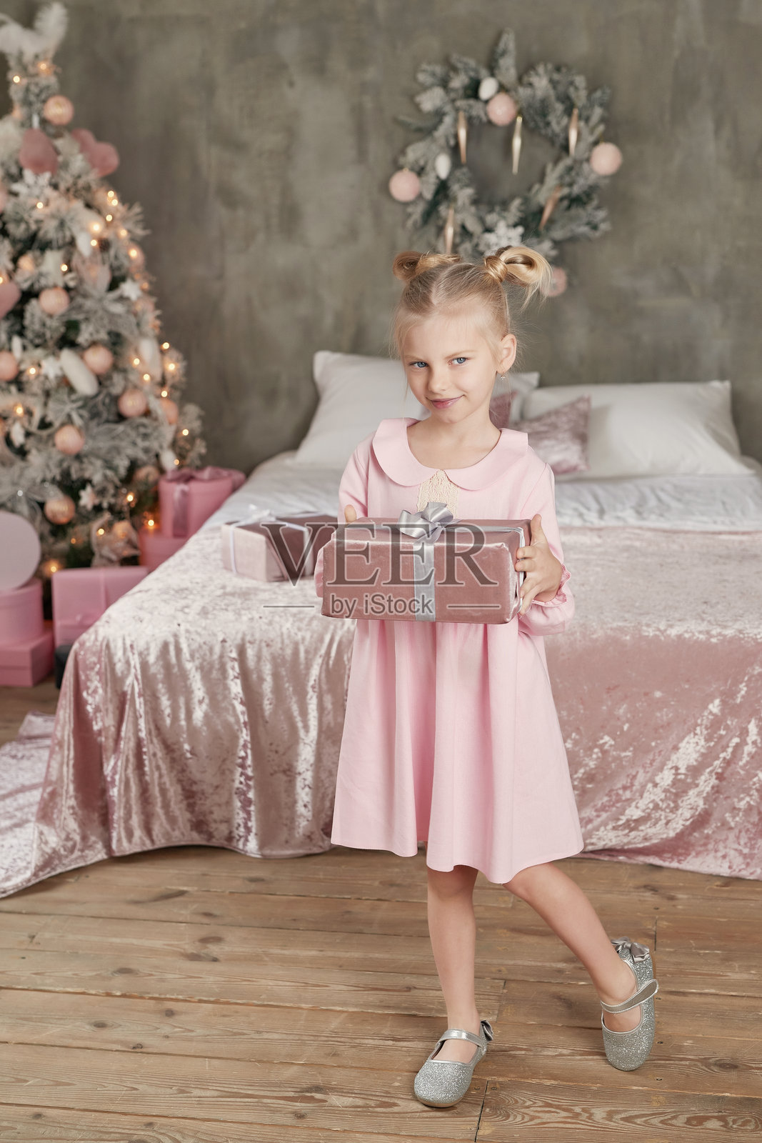 穿着粉色裙子的小女孩在圣诞树前拿着礼物。圣诞快乐，节日快乐！健康的宝宝和冬季概念。家庭圣诞。照片摄影图片