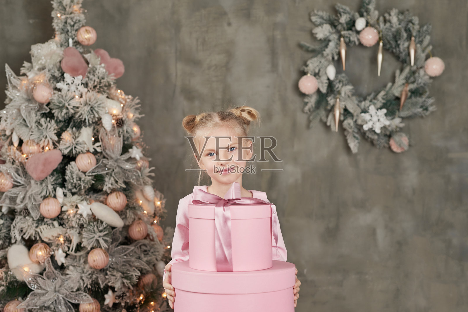 穿着粉色裙子的可爱小女孩在圣诞树前拿着礼物。圣诞快乐，节日快乐！健康的宝宝和冬季概念。家庭圣诞。照片摄影图片