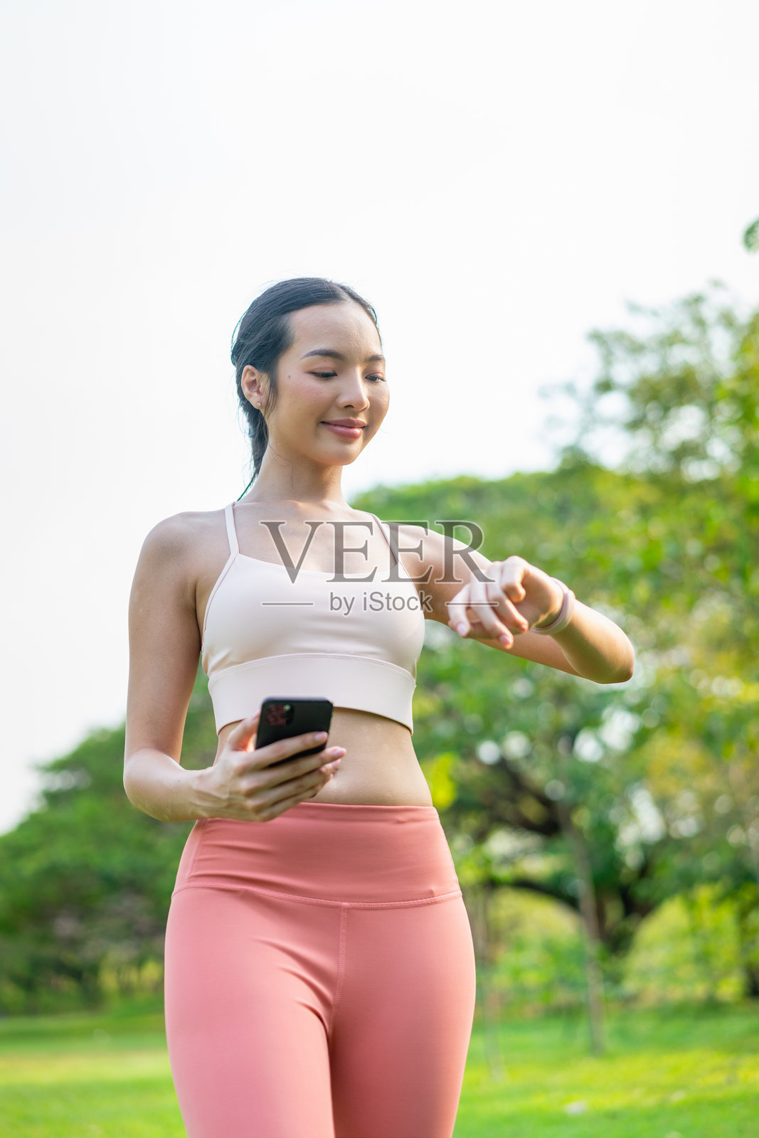 年轻亚洲女性在公园户外锻炼时使用手机和智能手表照片摄影图片