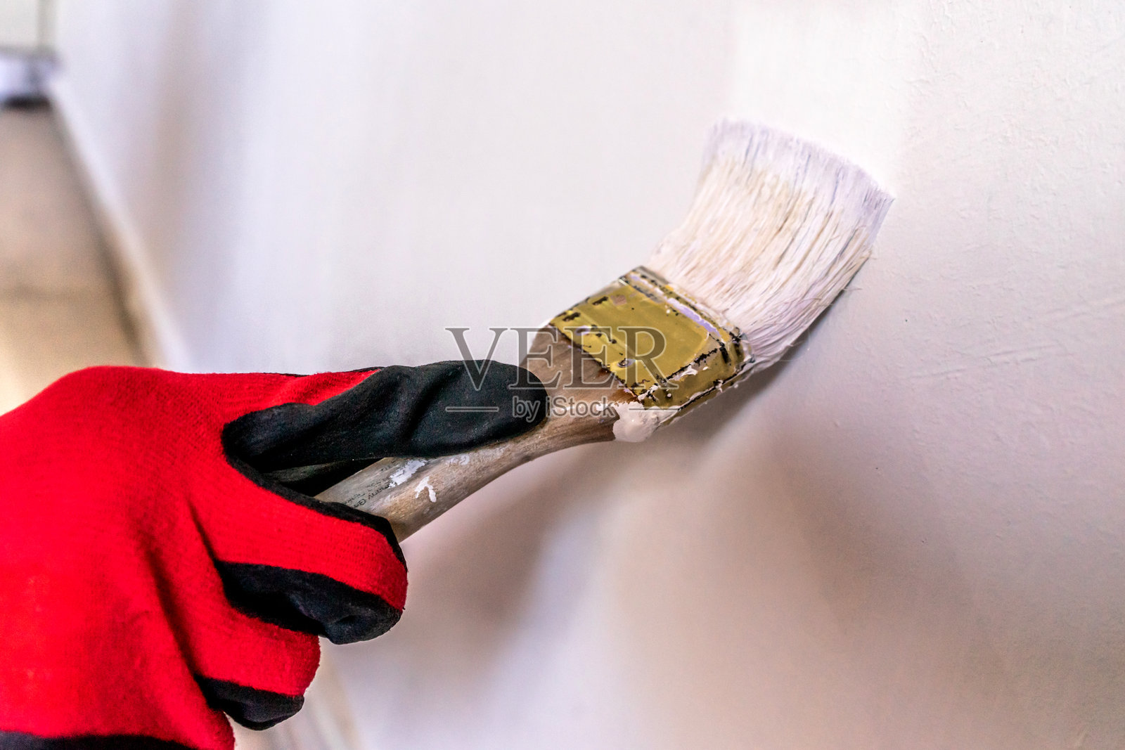 一名戴着手套的工人用刷子给门的边缘涂上白色油漆。照片摄影图片