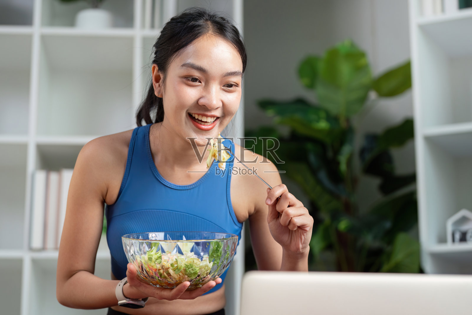 兴奋的女性在家中视频聊天时吃着健康沙拉。照片摄影图片