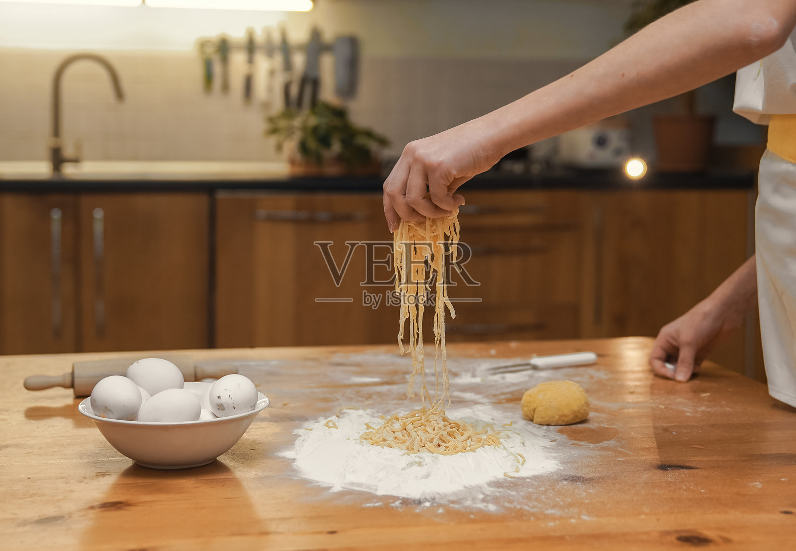 女孩在家制作自制面条，用擀面杖擀平面团，并用刀切割面团。照片摄影图片