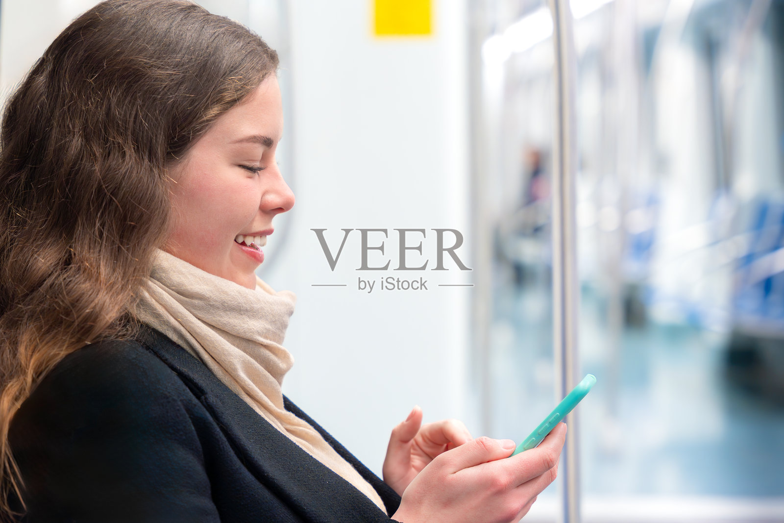 侧面视角的年轻女性在地铁上使用智能手机时开心地笑着照片摄影图片