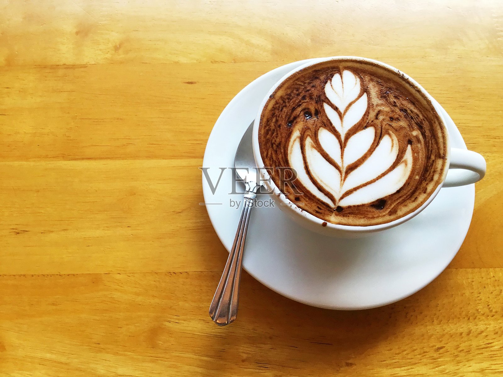 木桌上摆放着一杯带有拉花的咖啡。照片摄影图片