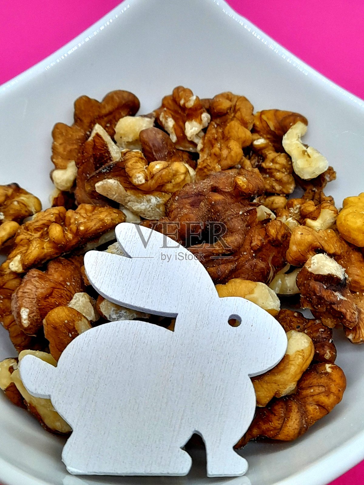 小碗里的核桃和粉色背景。照片摄影图片