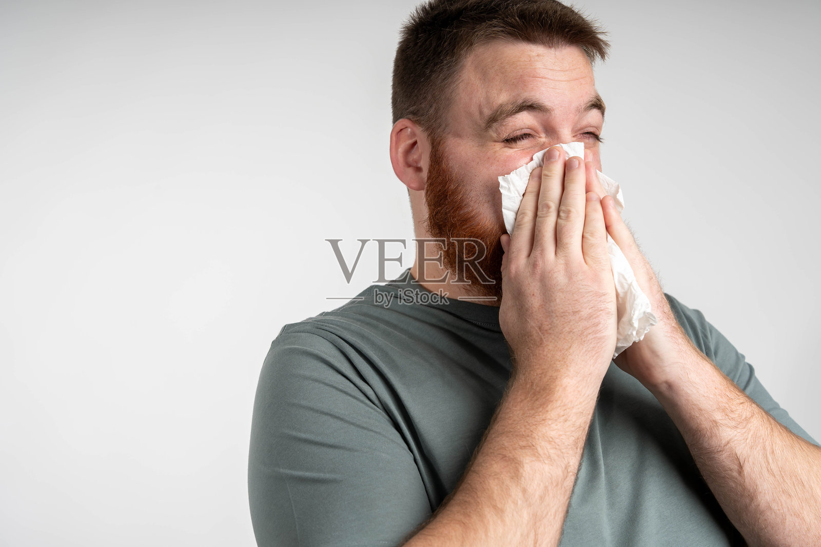 生病的胡子男人，流鼻涕，正在用纸巾，表现出流感症状。照片摄影图片