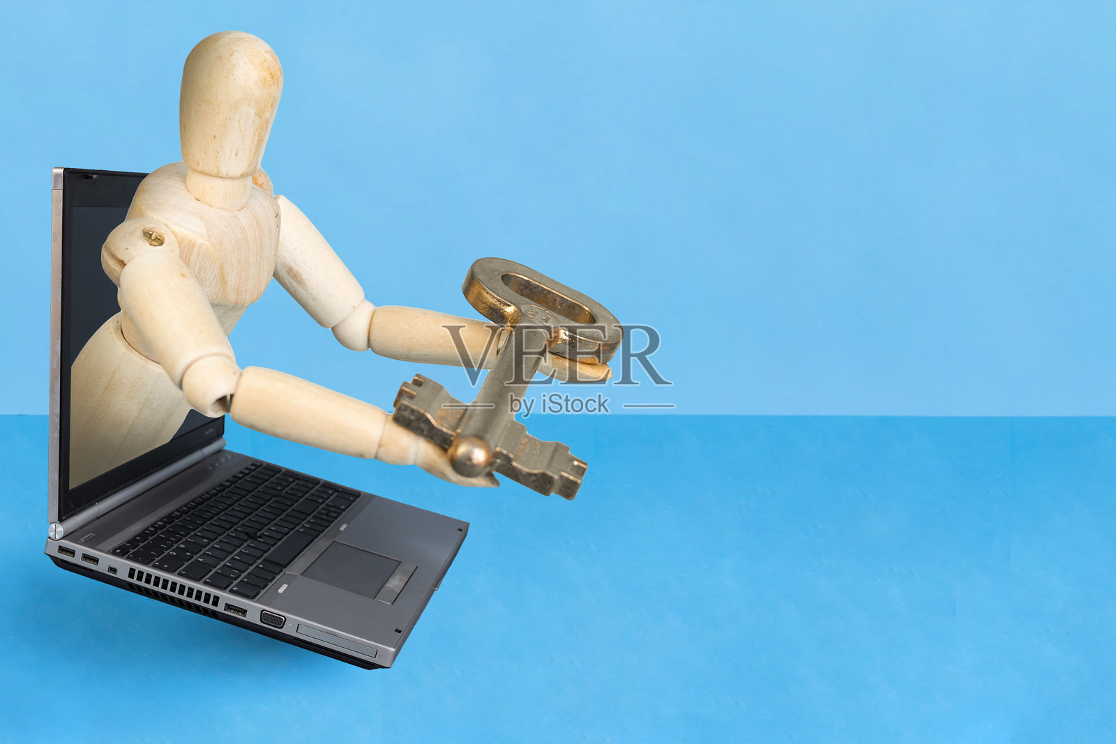 木制人偶从笔记本电脑屏幕中出现，手持金钥匙，背景为蓝色，互联网安全概念照片摄影图片