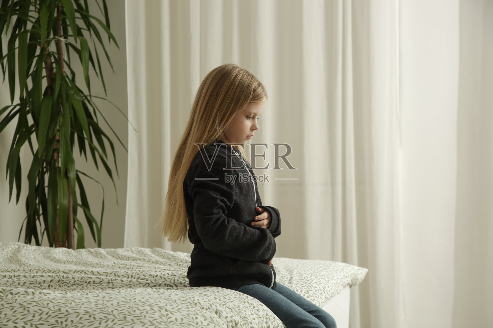 小女孩坐在卧室的床上，手放在肚子上，感到腹痛。照片摄影图片